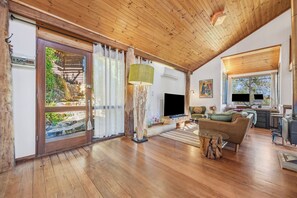 Een ruime woonkamer met houten vloer, een groene bank, een bijzettafeltje en een open haard.