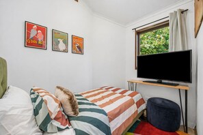 Een slaapkamer met een bed, een televisie en drie posters aan de muur.