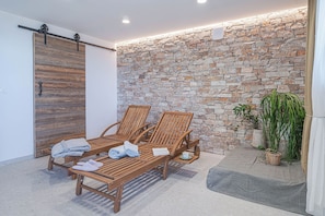 Un patio iluminado por el sol con sillones de madera, un muro de piedra y una puerta corredera.