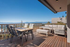Una terraza de madera con una mesa, sillas, un sofá y vistas a las montañas.