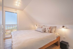Un dormitorio con cama, mesita de noche, lámpara de pared y vistas al exterior a través de una puerta.