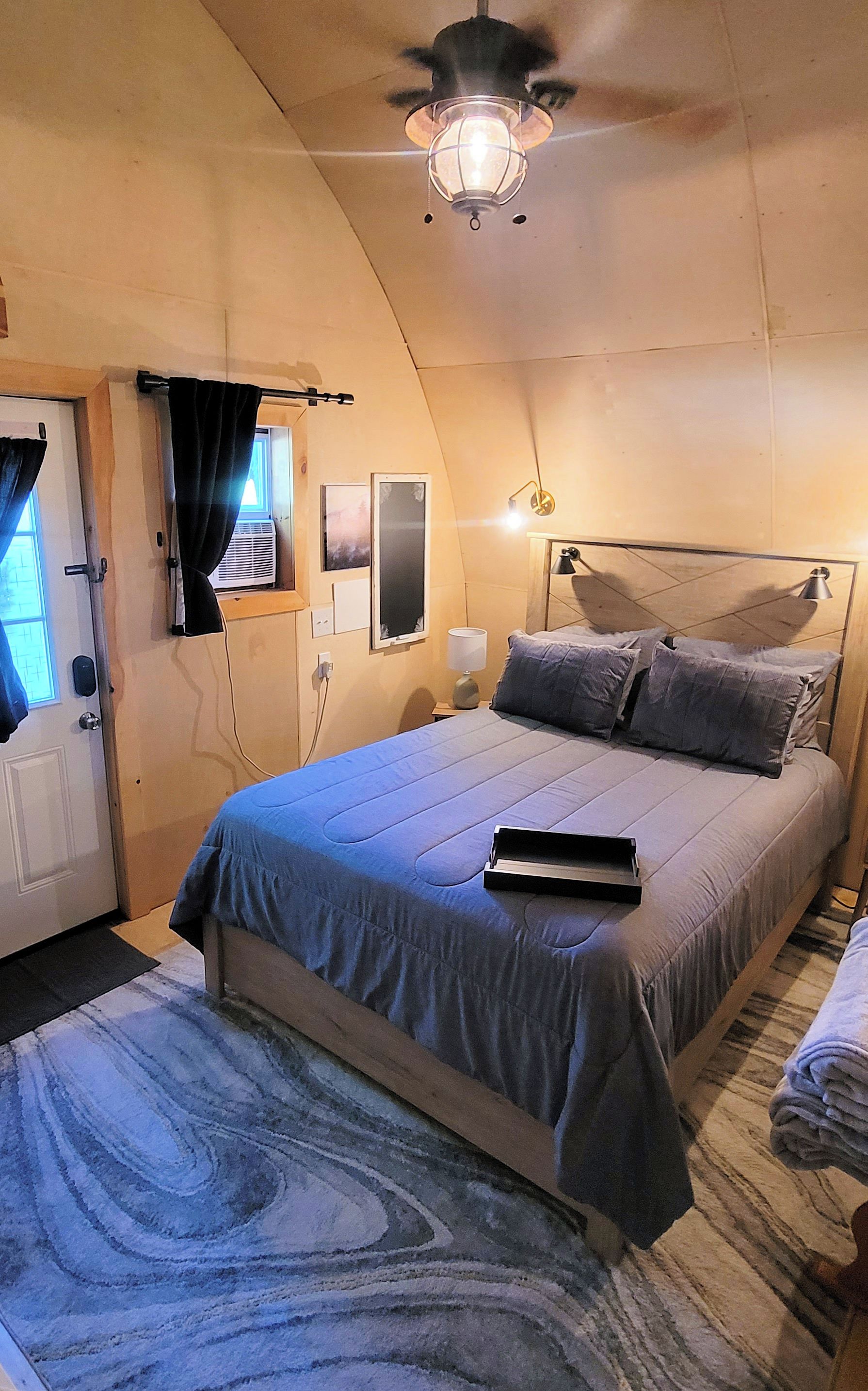 Ein Schlafzimmer mit einem Bett, Nachttischlampen, einem Deckenventilator und einem Fenster mit Vorhängen.