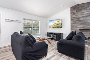 Een moderne woonkamer met een bank, een glazen salontafel, een flatscreen televisie aan de muur en een open haard.
