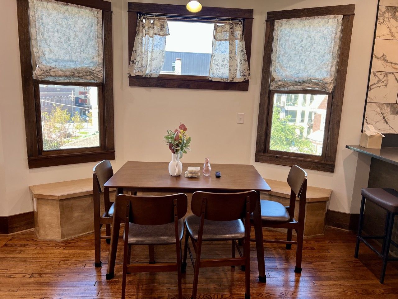 A dining area with a wooden table, four chairs, and a vase with flowers.