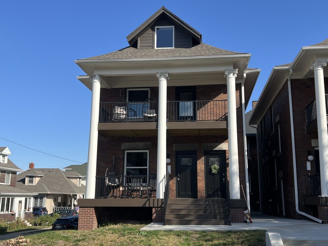 A two-story building with a balcony on the second floor, a front porch with chairs, and a brick facade.