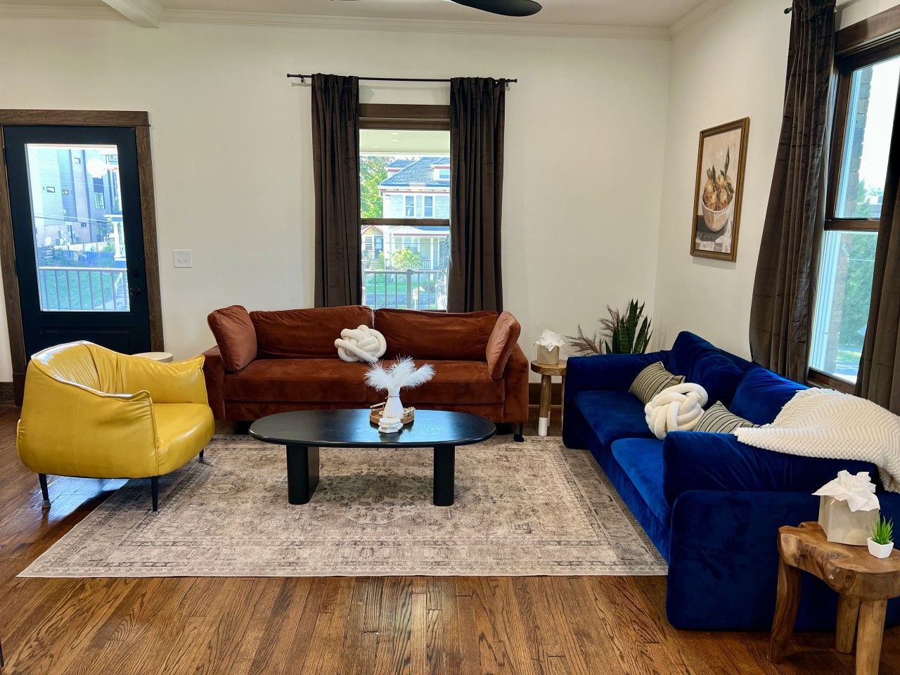 A living room with a brown sofa, a yellow armchair, a blue sofa, a coffee table, and a wooden floor.