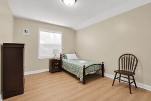 Um quarto com cama, mesa de cabeceira, cadeira e guarda-roupa.