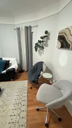 Una sala de estar con un sofá, un sillón gris, un tapete estampado, una estantería para plantas montada en la pared y un cuadro.