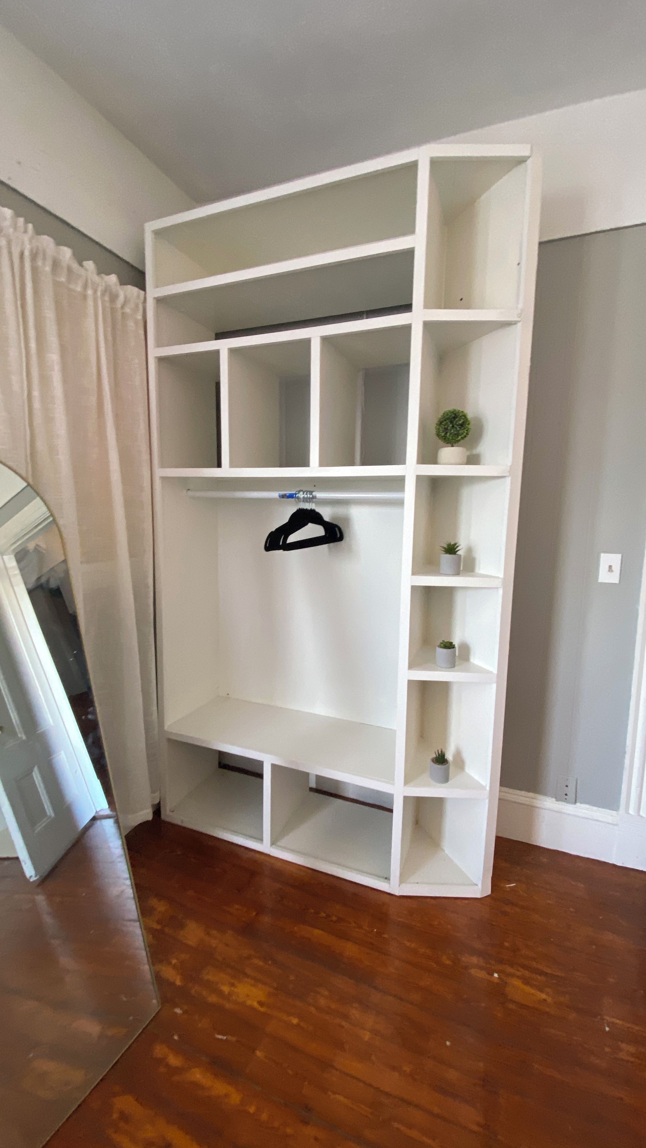 Un armario empotrado blanco con múltiples estantes y barra para colgar, ubicado en una habitación con piso de madera y puerta blanca.