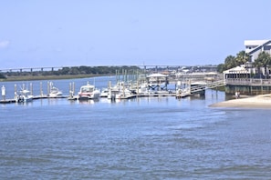 Ein Yachthafen mit vertäuten Booten, eine Brücke im Hintergrund und ein Gebäude im Vordergrund mit Strand.