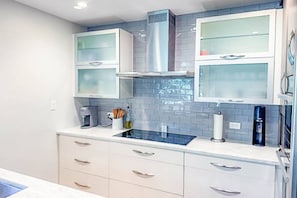 Eine moderne Küche mit weißen Schränken, einer Edelstahl-Dunstabzugshaube und einer blauen Spritzschutzwand.
