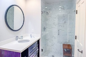 Une salle de bain avec un grand miroir rond, deux vasques, une douche à portes en verre et un meuble en bois.