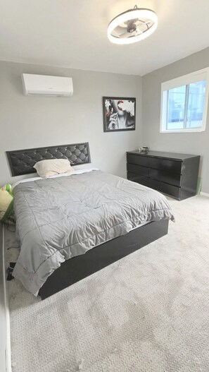 Een slaapkamer met een bed, een dressoir, een wandairconditioner, een schilderij en een raam.