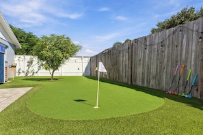 Ein Garten mit einem kleinen Putting-Grün, einem Holzzaun und einem Baum.
