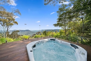 Ein Whirlpool auf einer Holzterrasse mit herrlichem Blick auf Berge und Bäume.