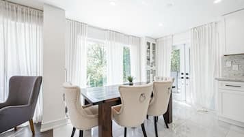 A modern dining area with a wooden table and four chairs, a grey armchair, and a kitchen with white cabinets and a marble backsplash.