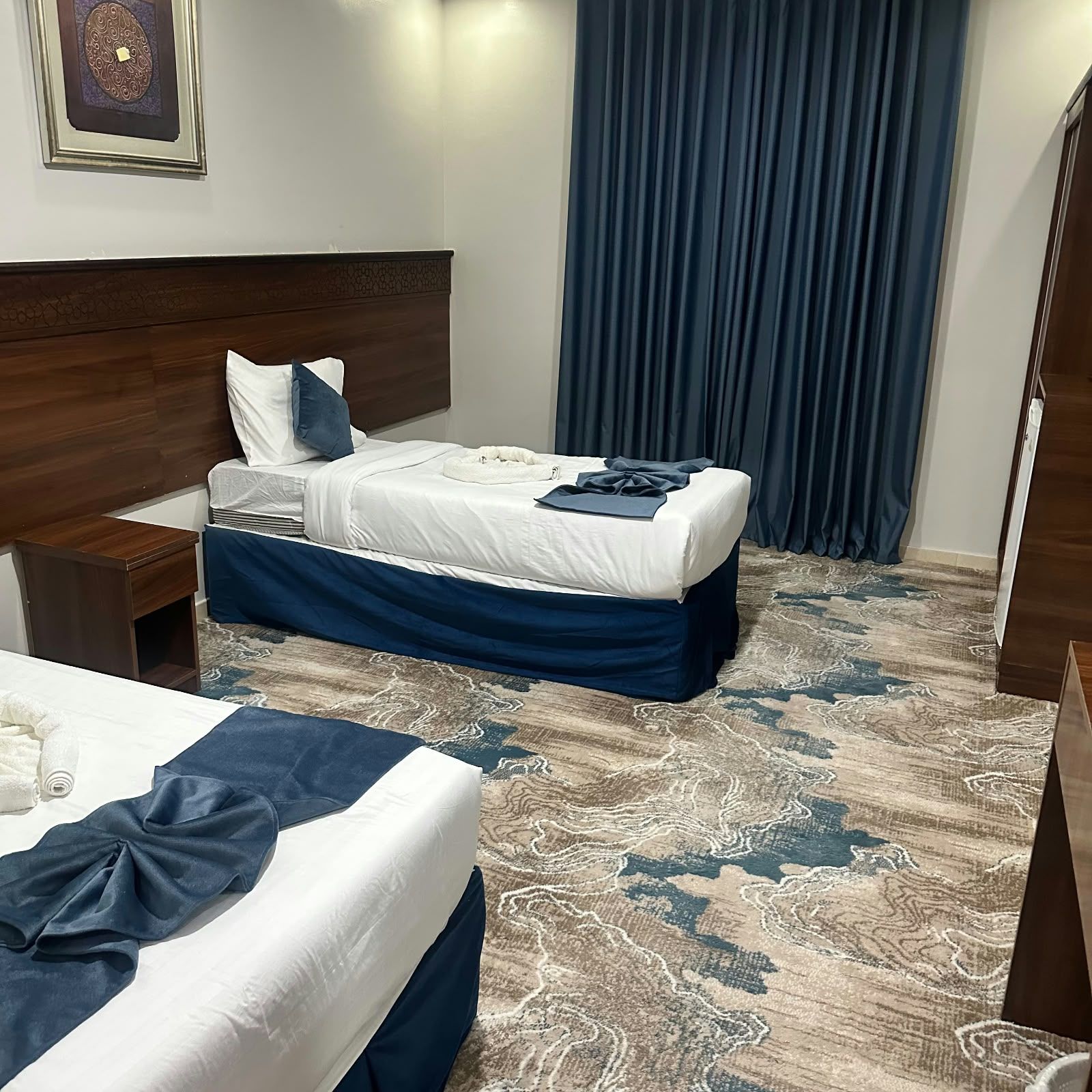 Une chambre d’hôtel avec deux lits, une tête de lit en bois, une moquette à motifs et une grande fenêtre avec des rideaux.