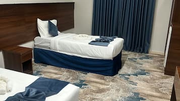 Une chambre d’hôtel avec deux lits, une tête de lit en bois, une moquette à motifs et une grande fenêtre avec des rideaux.