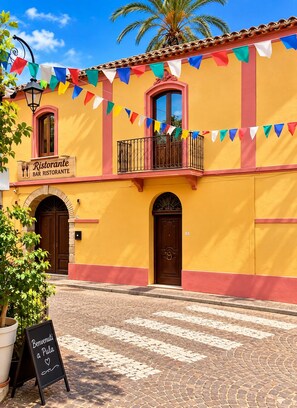 Um edifício amarelo com placa indicando bar e restaurante, uma varanda e uma rua de calçada.