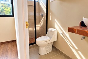 Un baño moderno con inodoro, zona de ducha y lavabo con dispensador de jabón.