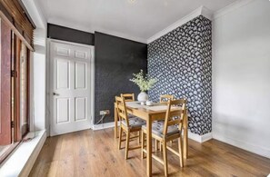A dining area with a wooden table and chairs, a white door, and a black and white patterned wall. - Modern & Bright - 1 Bedroom Flat (right in the center of Kingston Highstreet) (Kingston upon Thames)