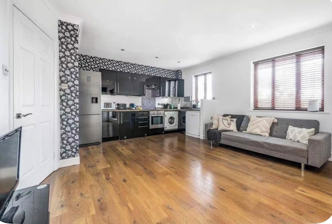 A modern kitchen with built-in appliances, a grey sofa, and a wooden floor.