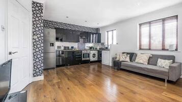 A modern kitchen with built-in appliances, a grey sofa, and a wooden floor.