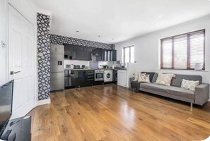 A modern kitchen with built-in appliances, a grey sofa, and a wooden floor. - Modern & Bright - 1 Bedroom Flat (right in the center of Kingston Highstreet) (Kingston upon Thames)