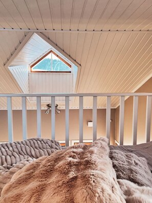 Ein Zimmer mit schrägem Dach, einem Fenster und einem Bett mit einer gemusterten Decke.