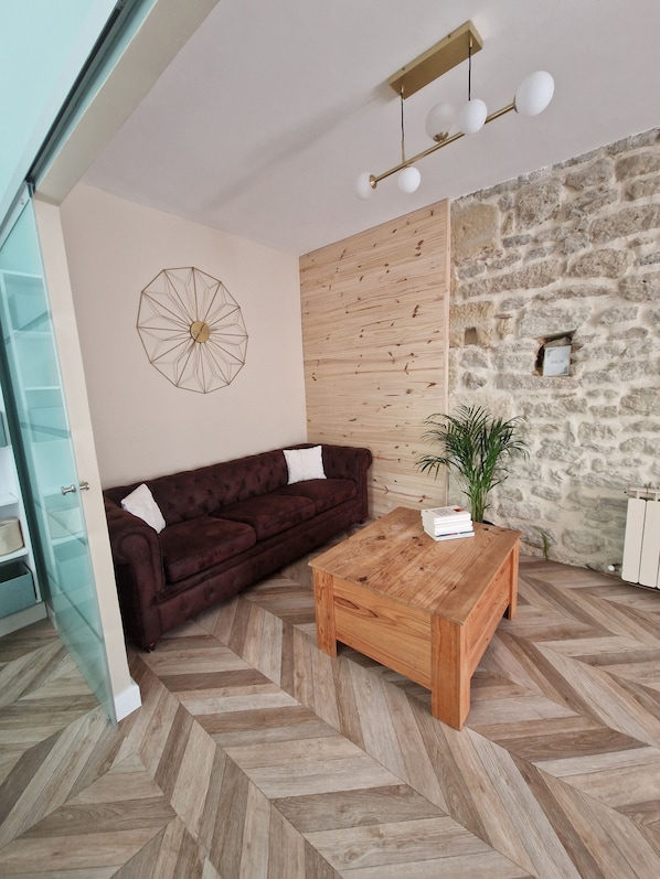 A modern living room with a herringbone-patterned floor, a brown sofa, a wooden coffee table, and a geometric wall decoration.
