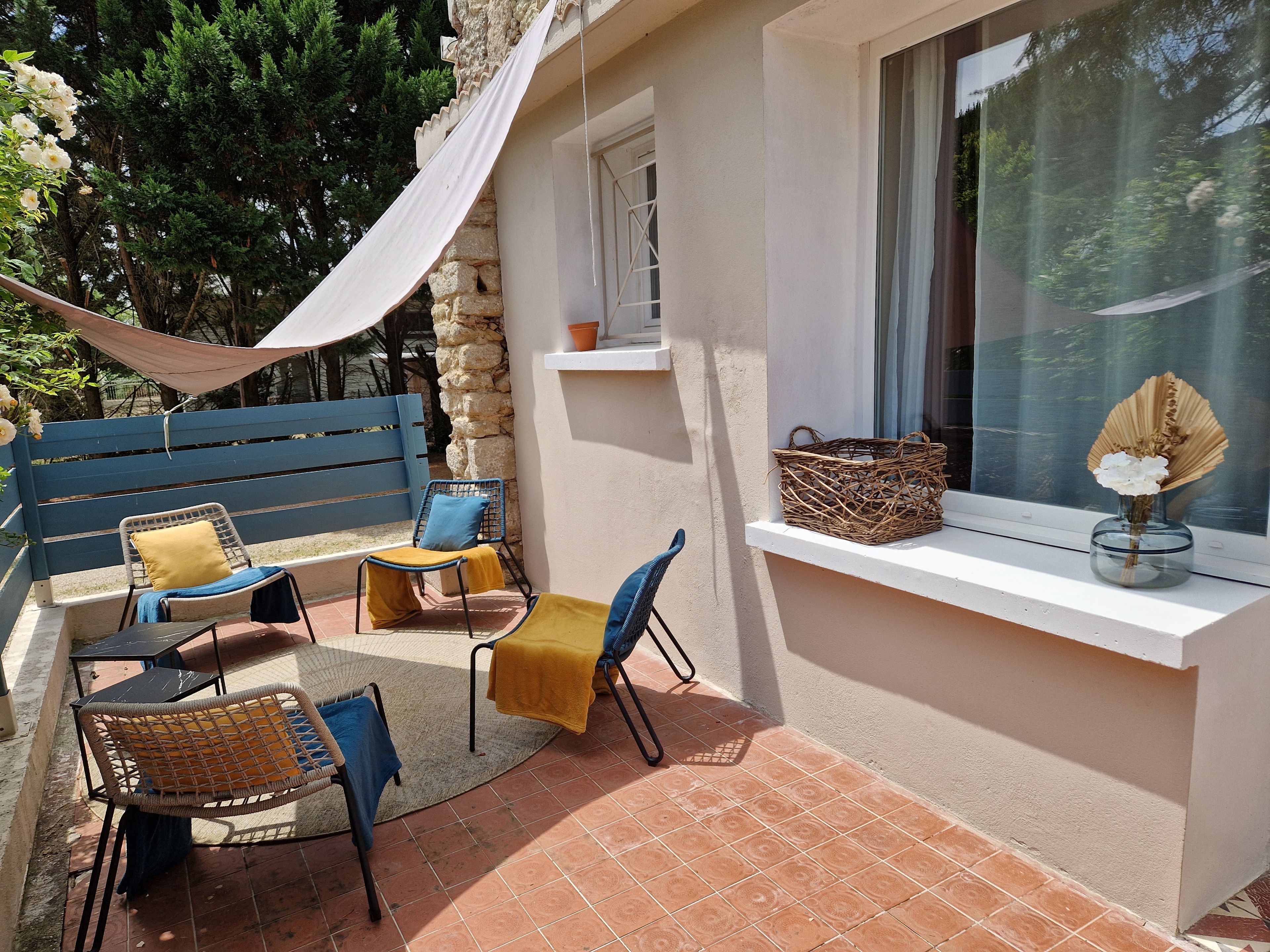 A patio with outdoor furniture, a stone wall, and a window with a basket and flowers.