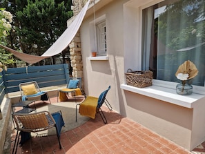A patio with outdoor furniture, a stone wall, and a window with a basket and flowers.