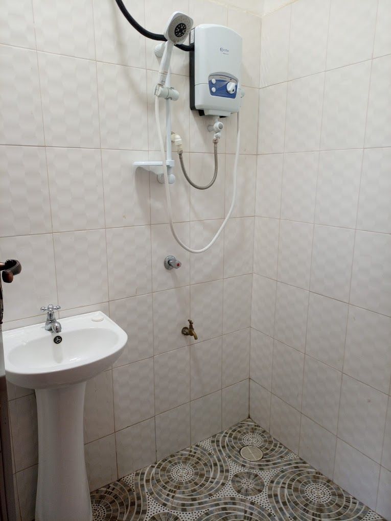 A bathroom with a white pedestal sink, a handheld showerhead, and a wall-mounted water heater.