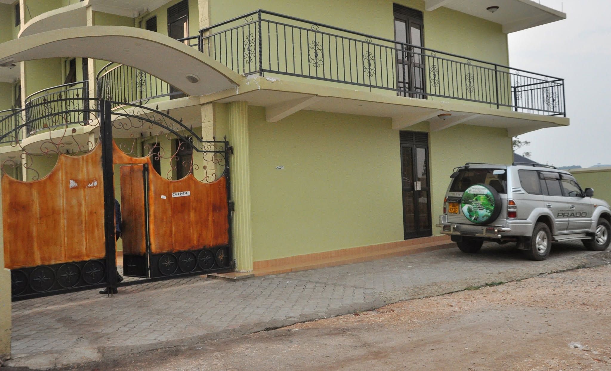 A two-story building with a gated entrance, a balcony with a metal railing, and a parked SUV.