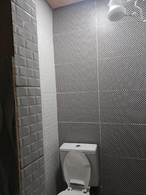 A bathroom with a toilet, a shower, and a tiled wall. - Santo Amaro inn (São Paulo)