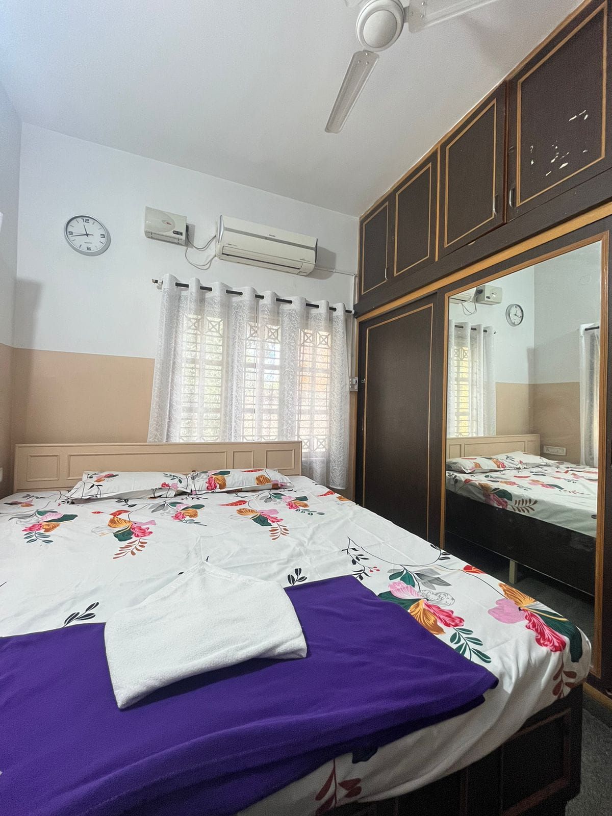 Un dormitorio con cama, armario, espejo, aire acondicionado y ventana con cortinas.