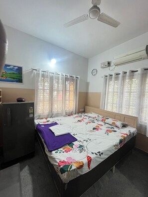 Une chambre à coucher comprenant un lit, un ventilateur de plafond, un appareil de climatisation, une horloge et un réfrigérateur.
