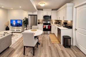 A modern kitchen with white cabinetry, stainless steel appliances, and a dining area with a round table and chairs. - 
Airport luxury 1 bed suite (Calgary)
