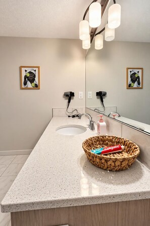 A bathroom with a double sink, a mirror, a towel rack, and a basket with toiletries. - 
Airport luxury 1 bed suite (Calgary)