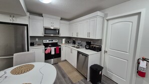 A compact kitchen with white cabinets, a microwave, a stove, a dishwasher, and a coffee maker. - 
Airport luxury 1 bed suite (Calgary)