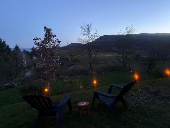 An outdoor seating area with chairs and a table, overlooking a hilly landscape.
