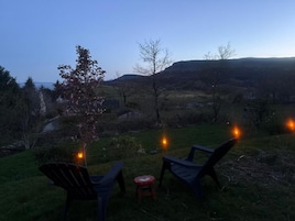 Área externa com assentos, cadeiras e uma mesa, com vista para uma paisagem montanhosa.