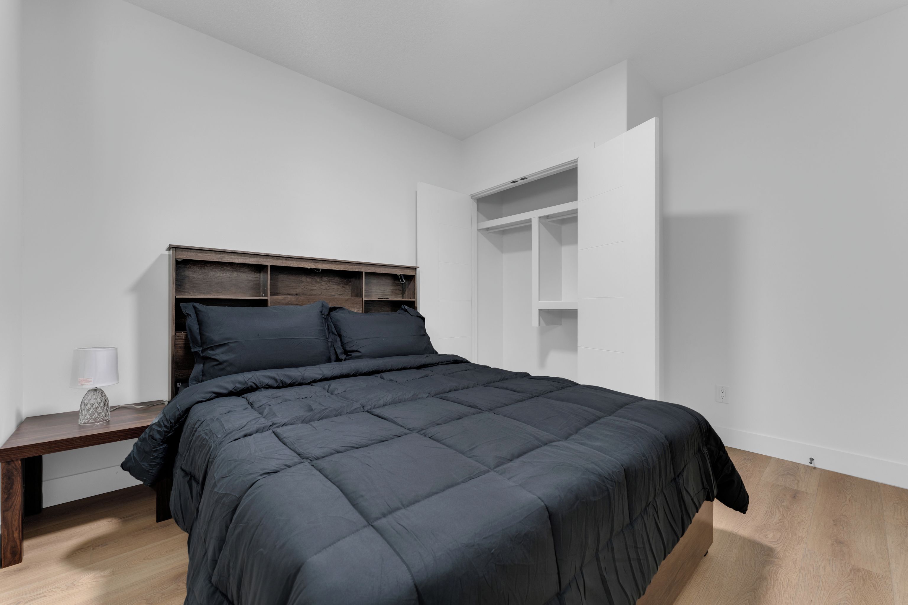 Een slaapkamer met een bed, nachtkastje, lamp en een inbouw wandplank.