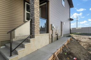 Une maison d’habitation avec une colonne en pierre, un escalier en béton et une terrasse en bois.