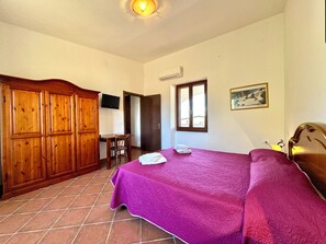 Une chambre à coucher avec un lit, une armoire en bois, un bureau avec une chaise, une télévision et une fenêtre.