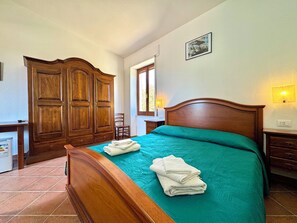 Une chambre à coucher avec un lit en bois, une grande armoire, une chaise et une fenêtre laissant entrer la lumière du jour.