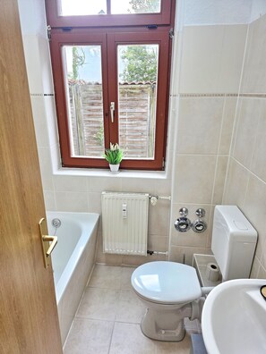 Ein Badezimmer mit Badewanne, Toilette und einem Fenster mit Ausblick nach draußen.