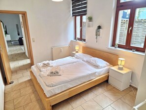 Ein Schlafzimmer mit einem hölzernen Bett, zwei Nachttischlampen, einem Heizkörper und einem Fenster mit Blick.