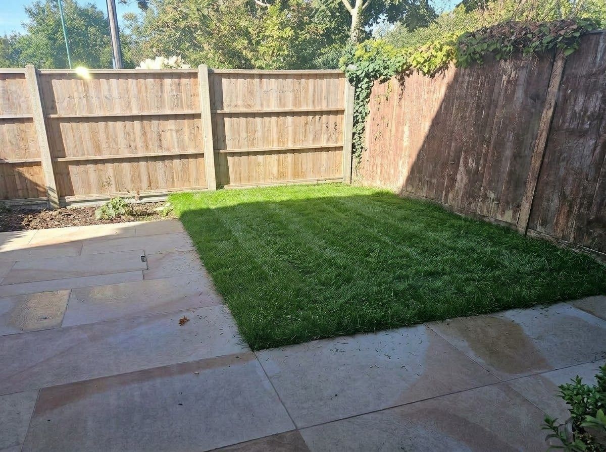 A backyard with a wooden fence, a paved patio, and a well-maintained lawn.