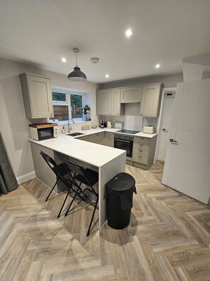 A modern kitchen with a central island, black chairs, a trash bin, and a window with a view. - 3 bedroom home in Horsham (Southwater)